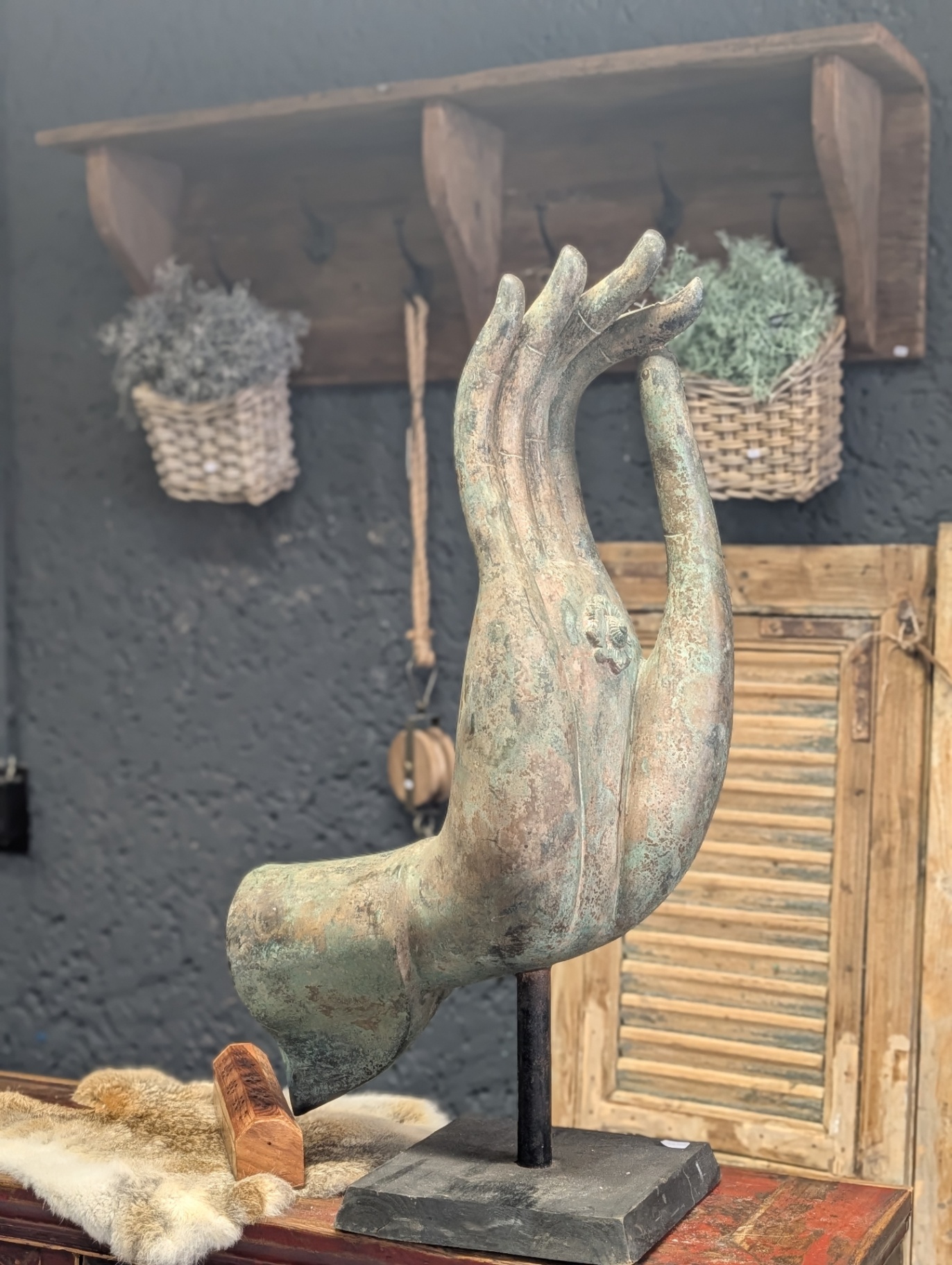 Bronzene Buddha-Hand-Skulptur auf Ständer vor dunkler Wand mit Wandregal aus Holz und Moos