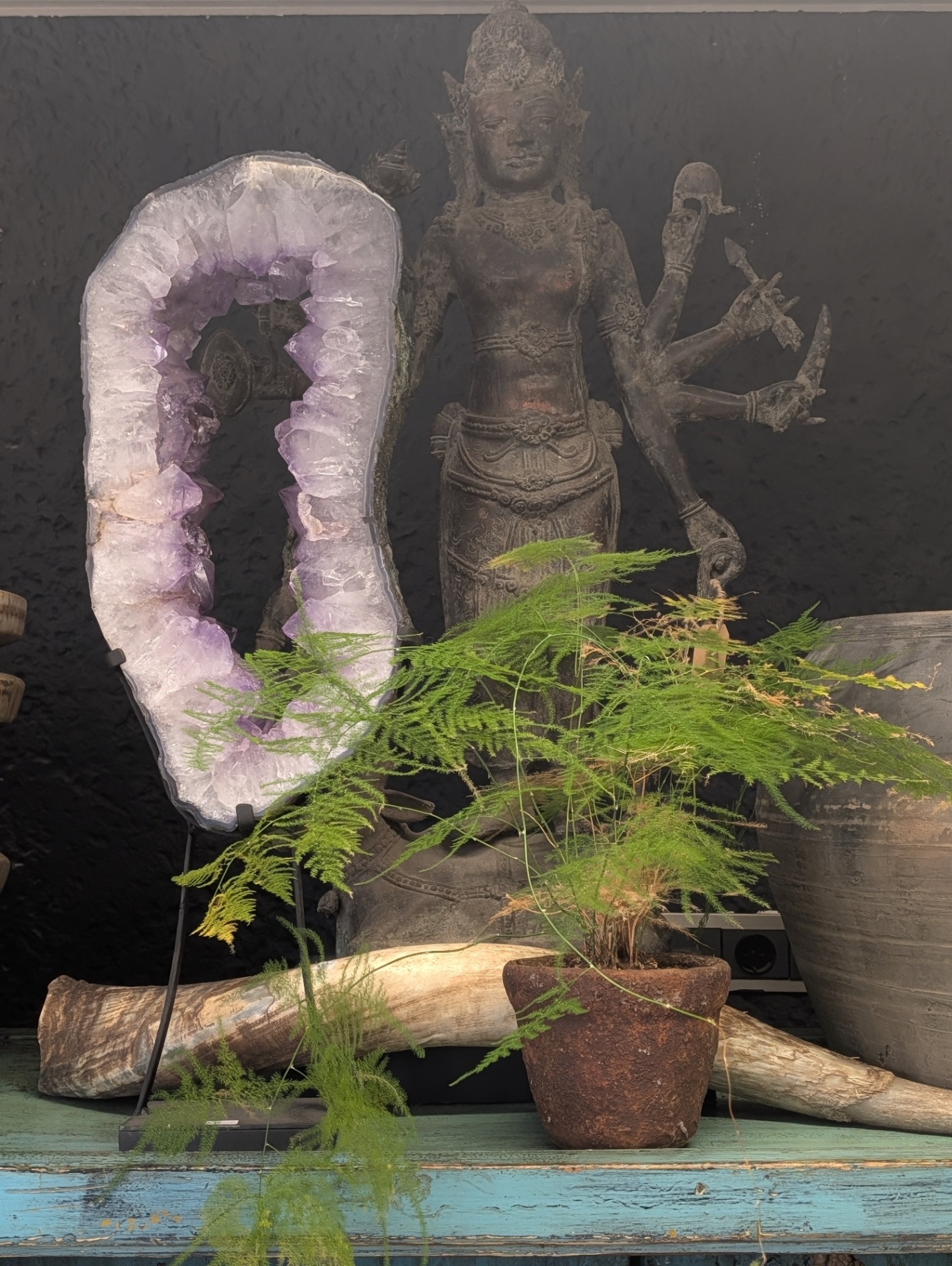 Amethyst-Geode vor Stein-Buddha mit Farn und alter Terrakotta-Topf im Showroom in Goirle