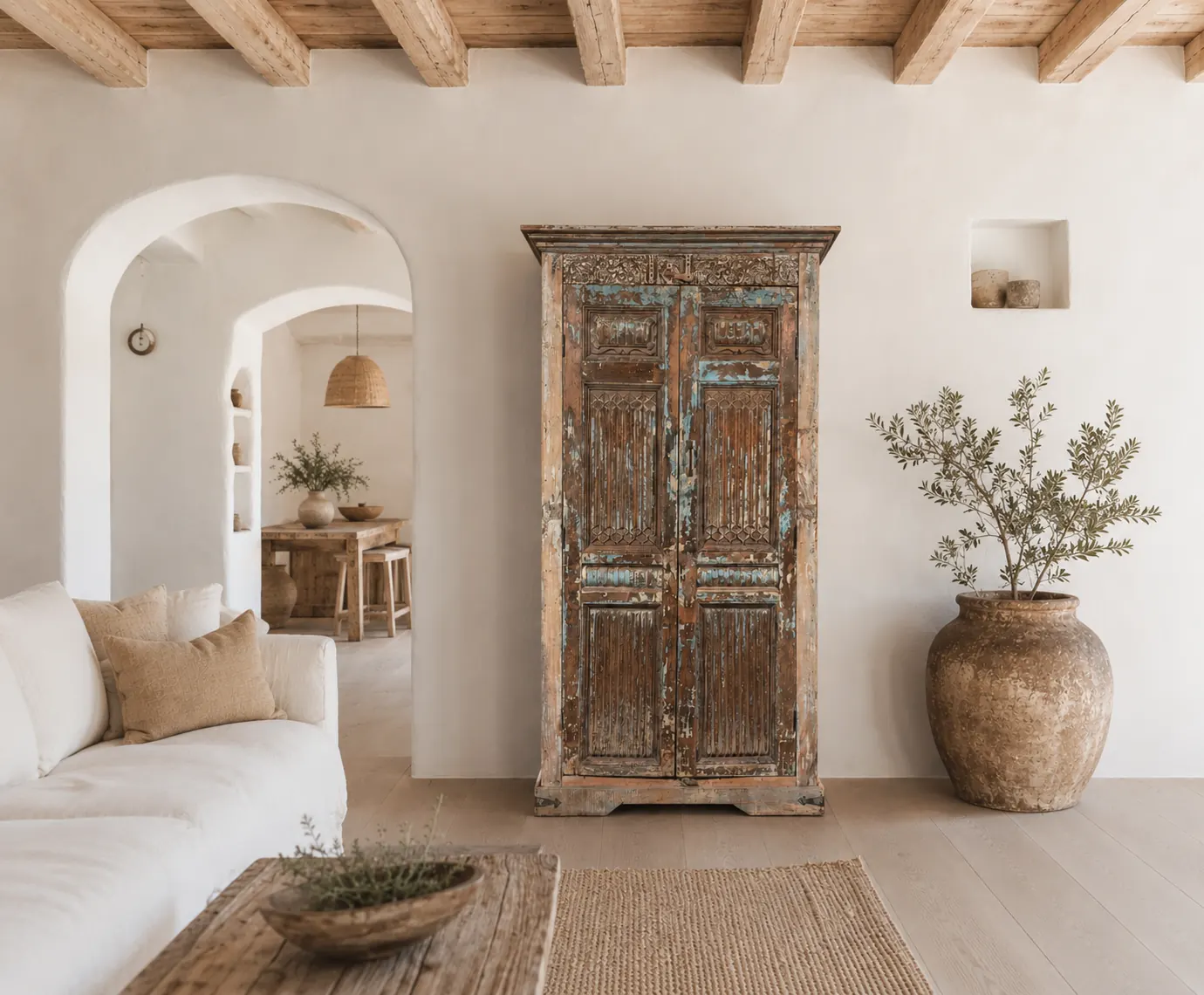 Ibiza-stijl vitrinekast van teakhout met glazen deuren in een bohemian en oosters interieur met olijftak, aardewerken kruiken en juten vloerkleed.