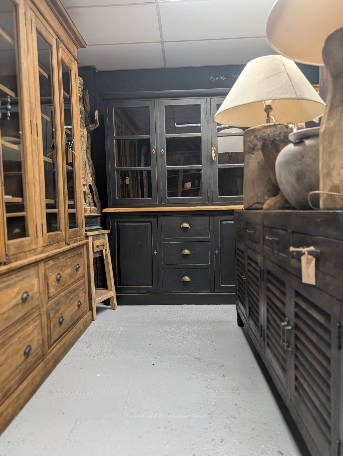 Durchblick durch den Showroom mit natürlicher Teak-Vitrine, mattschwarzem Buffetschrank und industriellem schwarzem Schrank