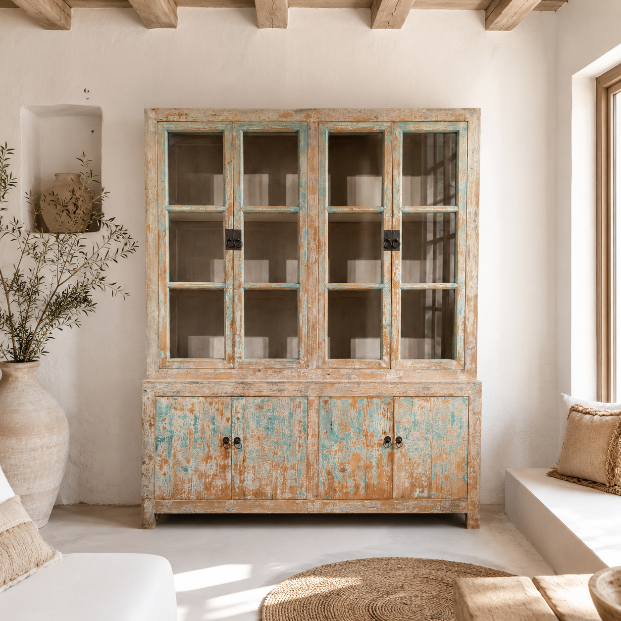 Vitrine patinée aux restes de peinture turquoise et portes vitrées contre un mur chaulé blanc dans un salon esprit Ibiza